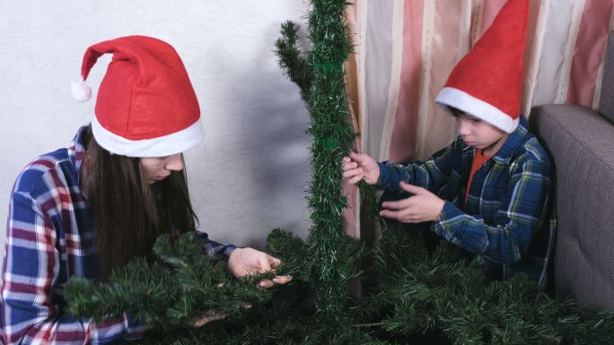 戴着圣诞帽的妈妈和儿子在家里安装圣诞树