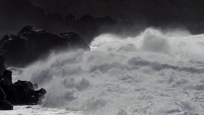 巨浪滚向岩石海岸。海浪拍打的浪花飞过