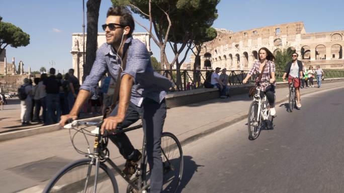 三个游客在罗马斗兽场附近道路上骑自行车