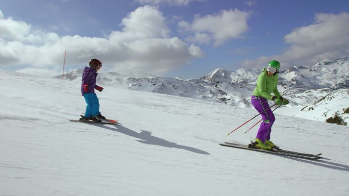 小女孩在她的滑雪教练/母亲后面滑雪