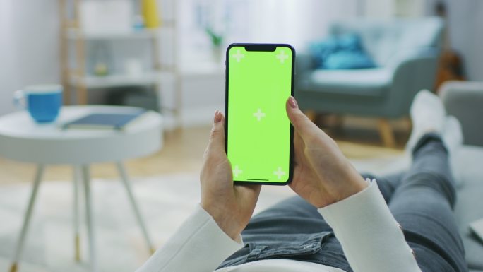 女人躺在沙发上使用绿色屏幕的手机