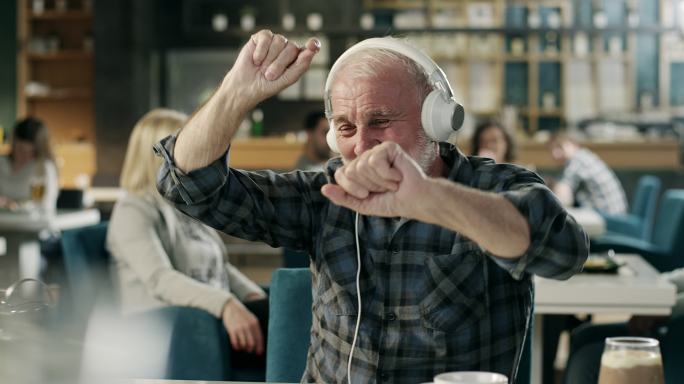 开朗的老人在餐厅用耳机听音乐