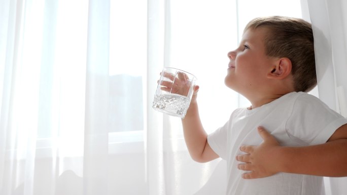 一个小男孩手里拿着一杯水在喝