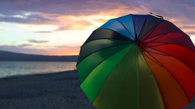 日落时分在沙滩上旋转彩虹伞的女人