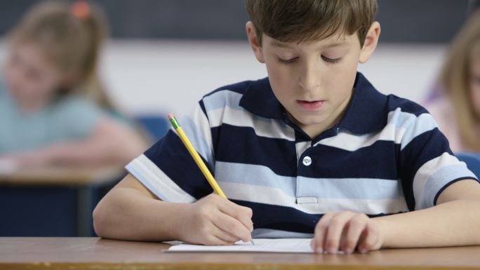 小学生在学校和他的同学用铅笔写字