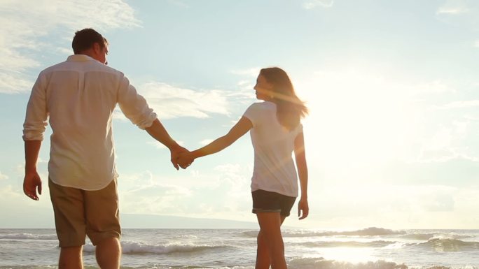 年轻夫妇手牵着手在日落时分的海滩上散步