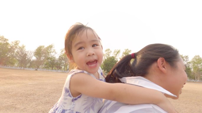 快乐的小女孩坐在妈妈的背上跑在公园里。