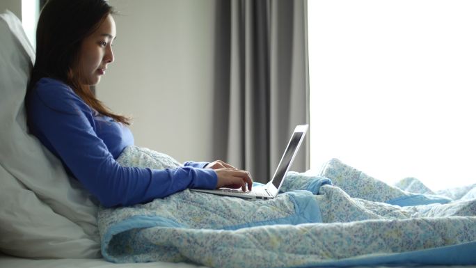 躺在床上的女人正在用笔记本电脑浏览网页