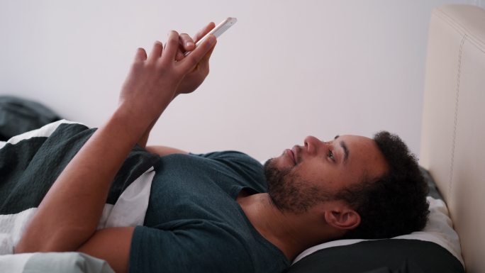 一个青年早上躺在床上手机聊天。