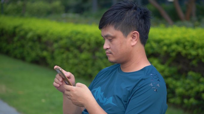 中年男性在小区公园绿道坐着玩手机4k视频