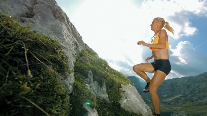 年轻女子在陡峭的岩石小道上跑上山