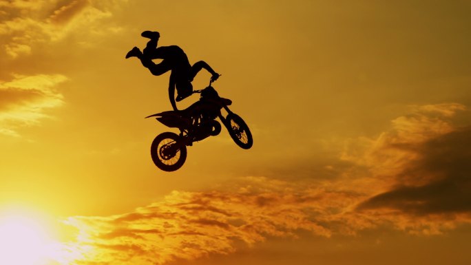 极限越野摩托车手在日落时跳跃表演特技
