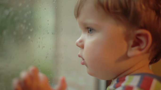 小男孩看着窗外在下雨