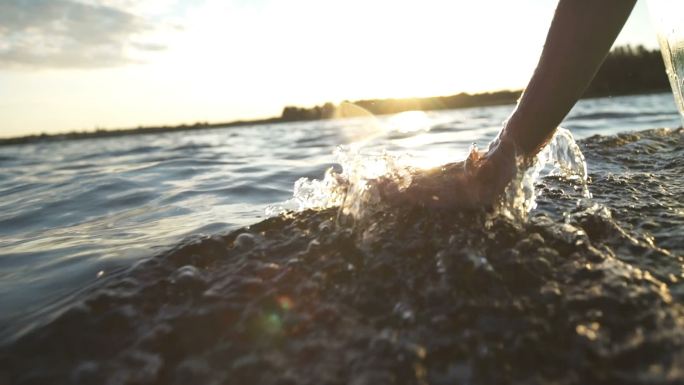 日落时，特写一个女孩在水中移动的手