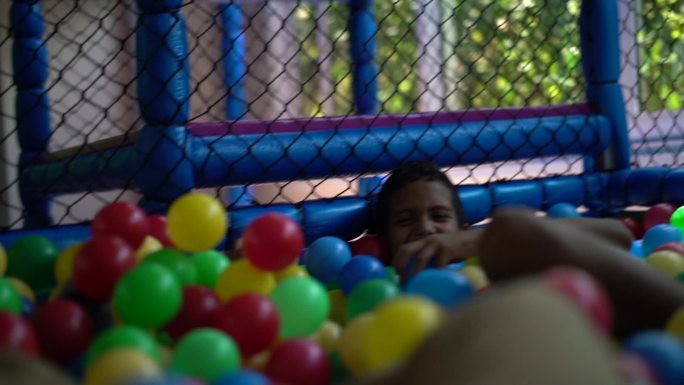 男孩在塑料池里玩五颜六色的球