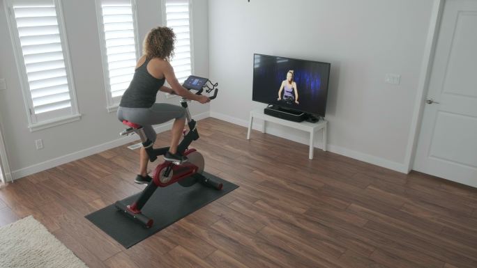 妇女在家里使用在线教练在旋转自行车上锻炼