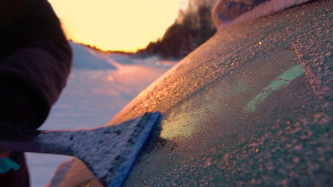 在冬季日出时刮掉车窗上闪闪发光的霜