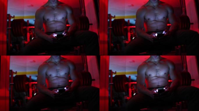 赤膊健美运动员在黑暗健身房使用手机