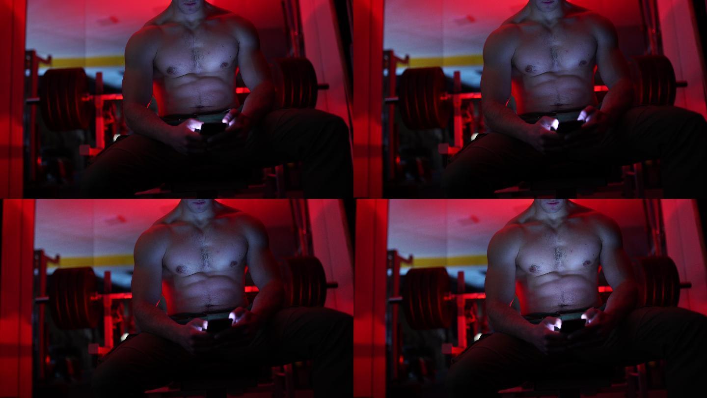 赤膊健美运动员在黑暗健身房使用手机