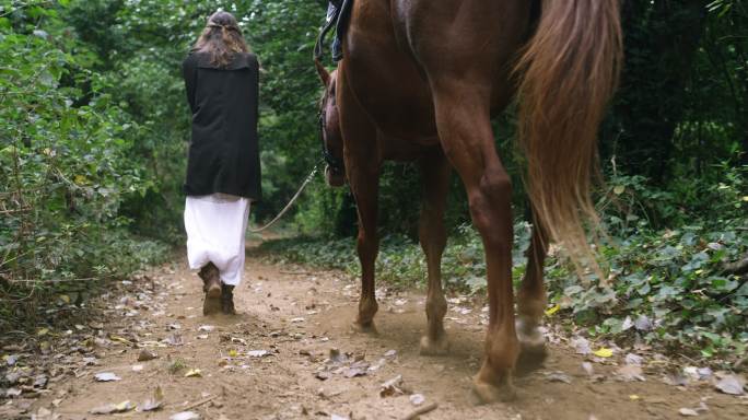 一个年轻女子在森林里牵着她的马行走