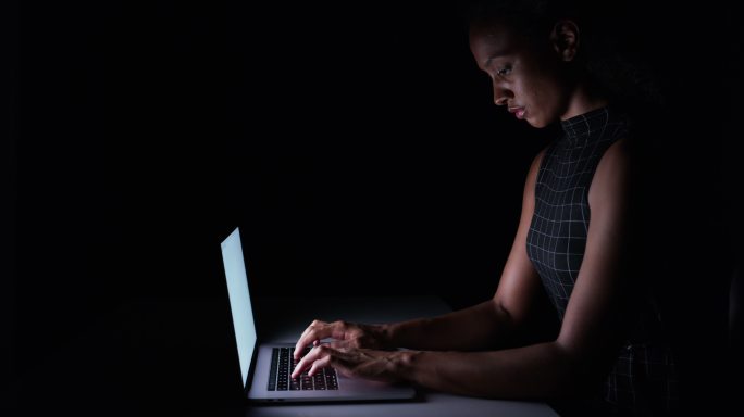年轻女子独自坐在黑暗中用笔记本电脑打字