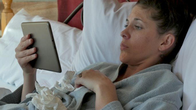 患流感的妇女在床上使平板电脑视频聊天