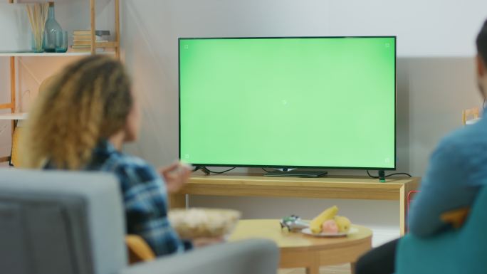 夫妇坐在家里的客厅里，看着绿色的彩色键屏幕电视