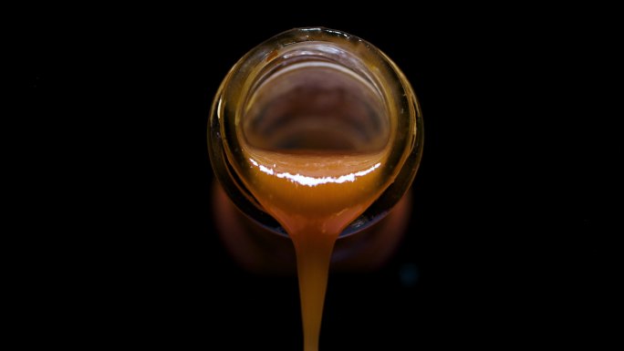 辣椒酱从一个玻璃瓶倒出的前视图，黑色背景