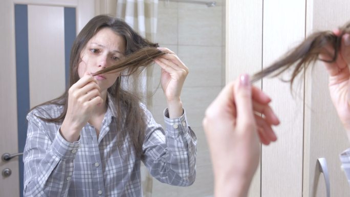 女人在浴室里看着她干枯、脆弱的头发。