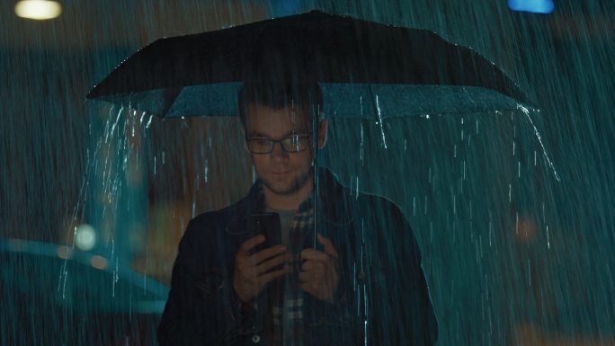 雨夜里，年轻人撑伞发短信