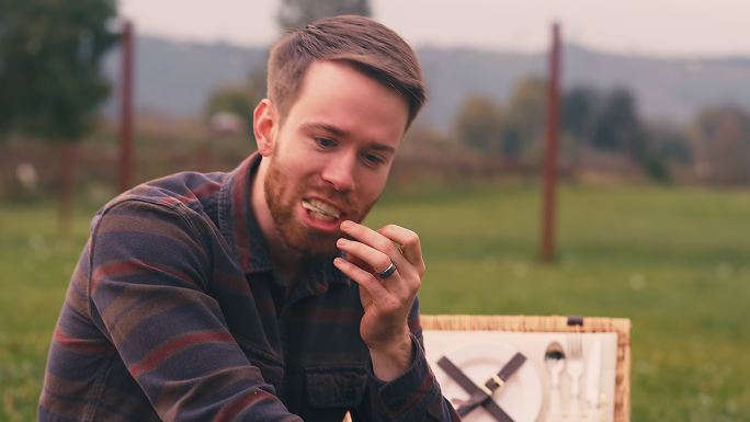 一个微笑的年轻人在秋天的野餐中吃奶酪