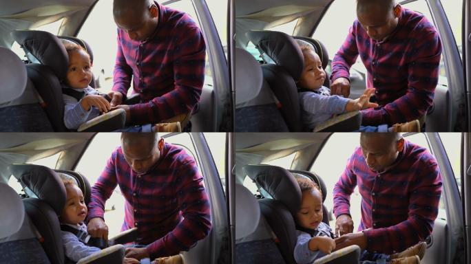 男孩坐在婴儿座椅上，父亲系着安全带