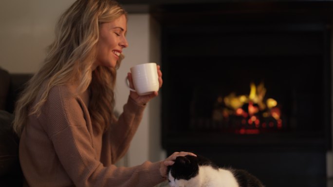 年轻女子一边喝咖啡，一边和她的猫玩