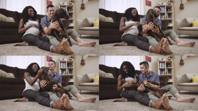 怀孕的妻子和丈夫坐在地板上和他们的狗玩耍