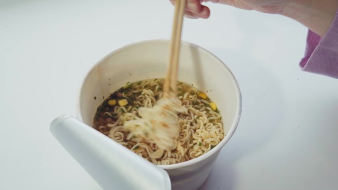 用筷子在纸碗里搅拌方便面