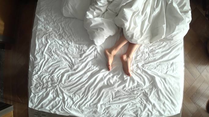 从上方看床上的女性腿，白色床上用品