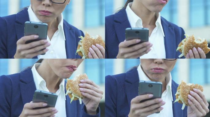 女人一边用手机一边吃汉堡