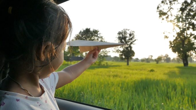 可爱的小女孩在车窗外玩纸飞机