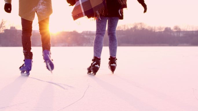 情侣手牵手在阳光明媚的冰冻湖面上滑冰。