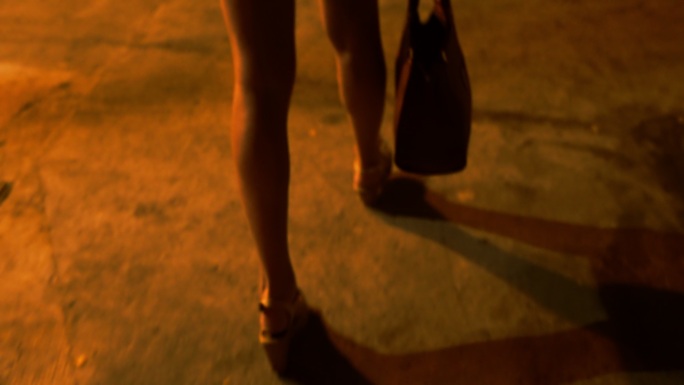 一名年轻女子在晚上提着包走在街上。