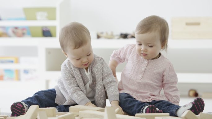 双胞胎坐在地上玩积木玩具