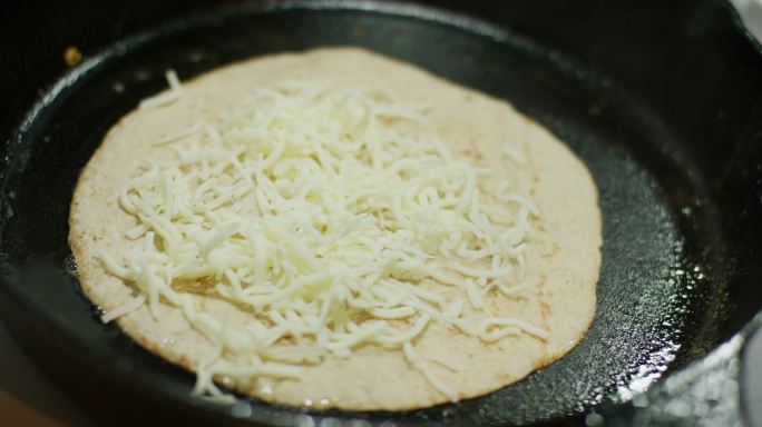 将磨碎的马苏里拉奶酪洒在玉米饼上