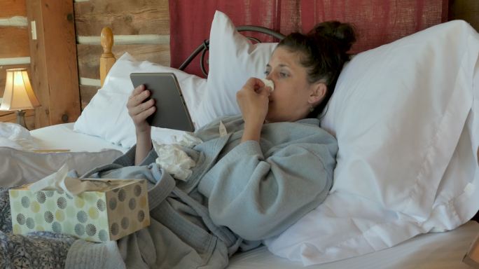 咳嗽流鼻涕的妇女在床上用平板电脑视频聊天