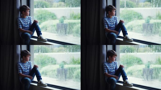 一个小男孩在家透过窗户看雨