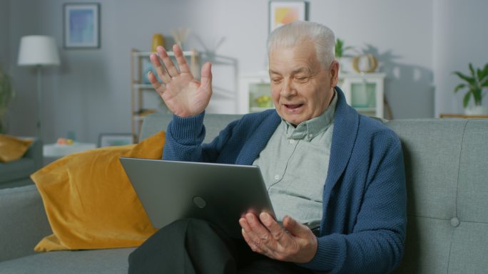 老人坐在沙发上用笔记本电脑打视频电话。