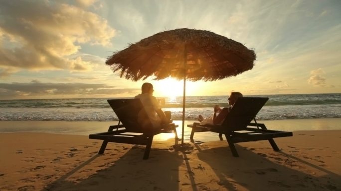 日出时，男人给坐在海滩边的女人端饮料
