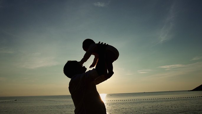 父亲日落时在热带海滩上玩耍和抱着儿子。