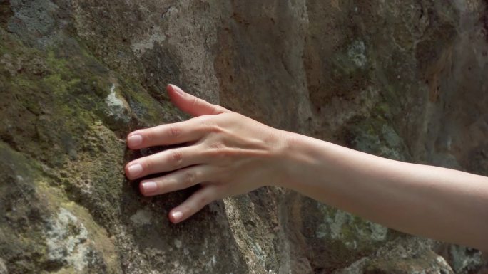 女性手触摸岩石粗糙表面。