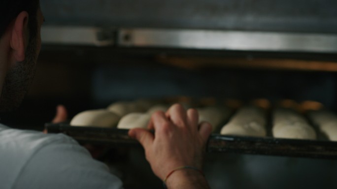 面包师将面团放入烤箱烘焙。