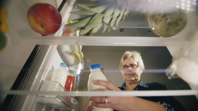 女士从冰箱里拿出牛奶，检查产品的保质期。